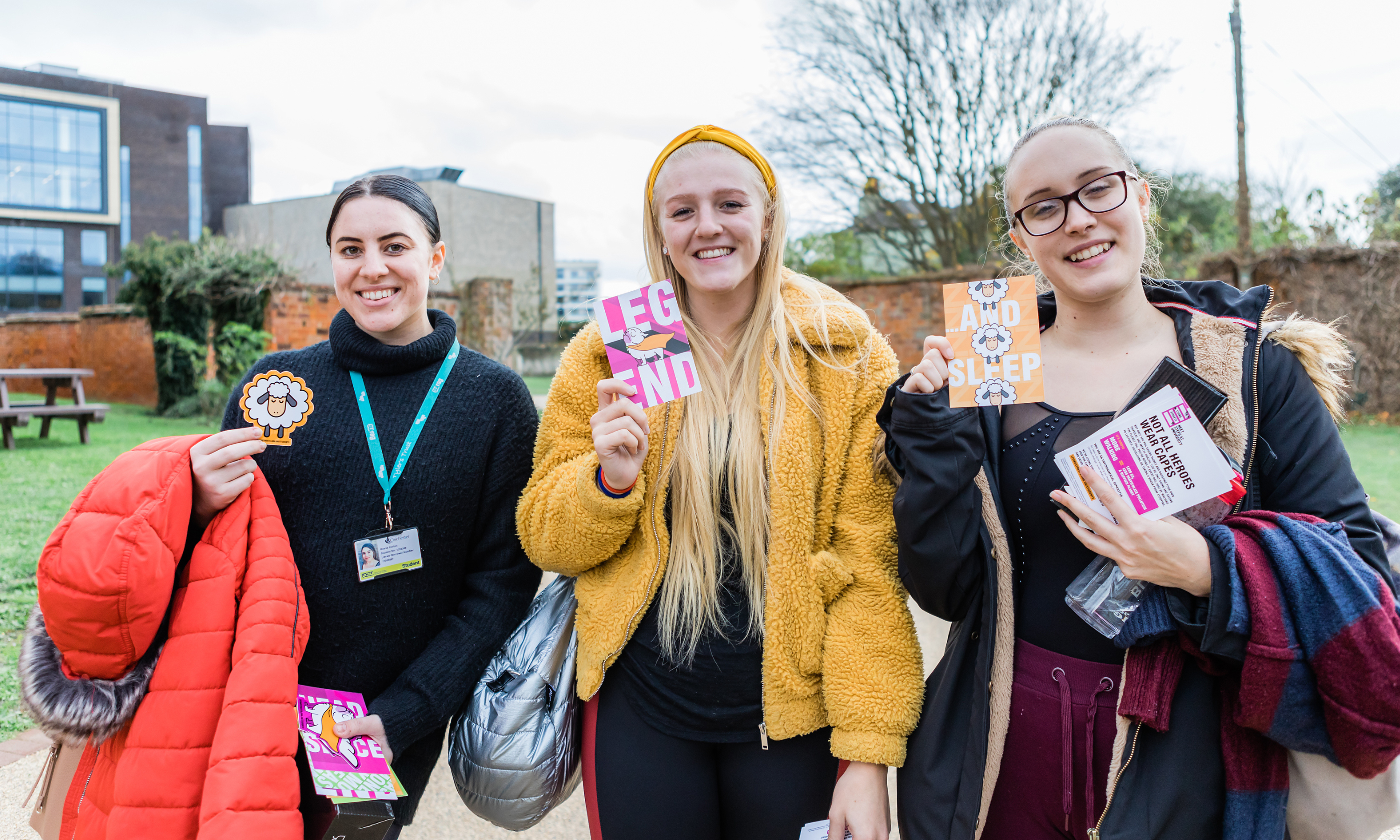 three female students holding up living streets merch and smiling