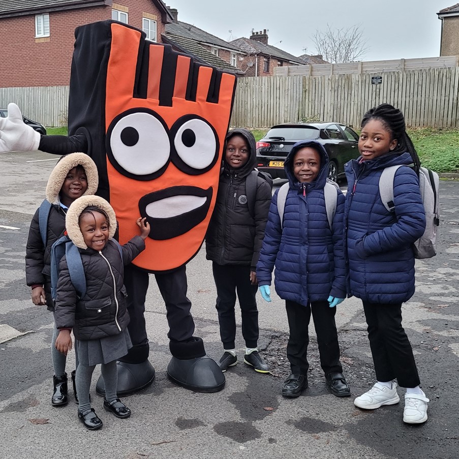 Five primary school aged pupils are stood with Strider, an orange foot-shaped mascot