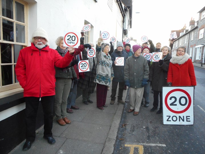 group of people holding up 20 mile an hour zone placards